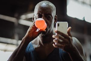 Brawny man drinking sports drink while checking phone during a workout session.